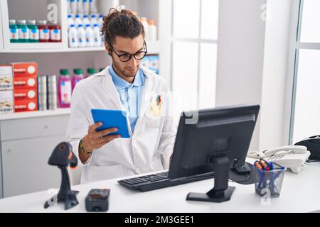 Junger hispanischer Apotheker mit Touchpad und Computer, der in der Apotheke arbeitet Stockfoto