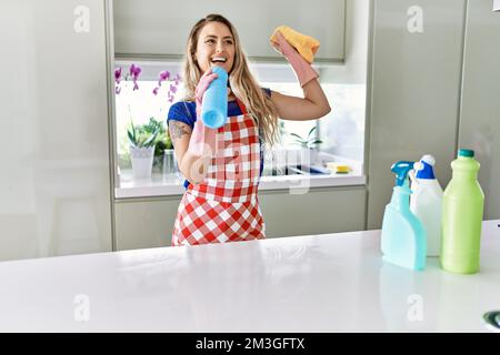 Junge Putzfrau singt mit Waschmittelflasche als Mikrophon in der Küche Stockfoto