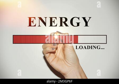Weibliche Hand mit glitzernden Nägeln, die die Ladeleiste mit dem Text „Energie“ zeigt Stockfoto