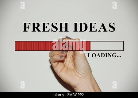 Weibliche Hand mit glitzernden Nägeln, die die Ladeleiste mit dem Text „Fresh Ideas“ zeigt Stockfoto