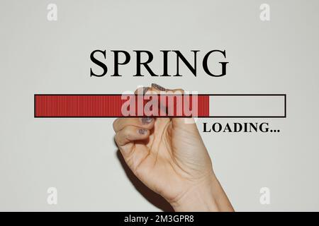 Weibliche Hand mit glitzernden Nägeln, die die Ladeleiste mit dem Text „Spring“ zeigt Stockfoto