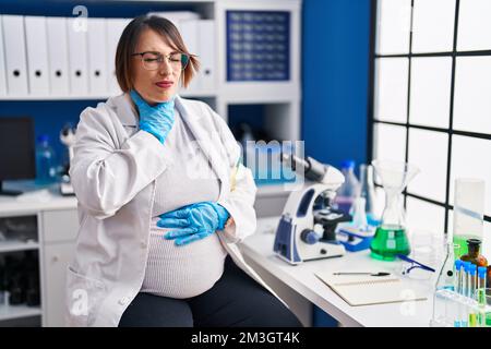 Schwangere Frau, die in einem Wissenschaftlerlabor arbeitet, berührt schmerzhaften Hals, Halsschmerzen wegen Grippe, Blutgerinnsel und Infektion Stockfoto