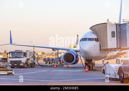 Passagierflugzeug parkt am Flughafen. Betankung bei Sonnenuntergang. Tankfahrzeug mit Kerosin. Abfertigung und Vorbereitung des Abflugs Stockfoto