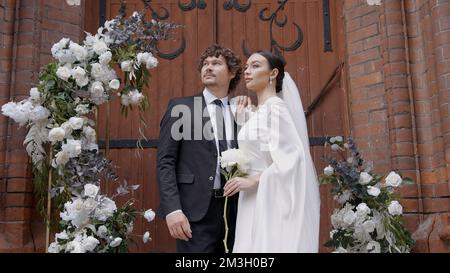 Ein helles und spektakuläres Hochzeitspaar. Action. Frischvermählte, wo eine Braut in einem weißen Kleid mit einem Schlitz am Bein und ein Mann mit einem Bart im Anzug walki Stockfoto