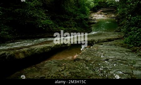 Schwirrende Bäche in den Bergen. Kreativ. Wasser fließt über die schwammigen hohen grünen Bäume, die den Fluss bilden, und Wanderreisende sind sichtbar Stockfoto