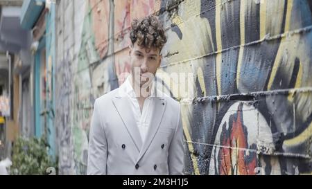 Wunderschöne Porträts neben der Graffiti-Mauer. Action. Stilvolle Leute, die an Straßenkunst-Schießereien mit einer Wand mit leuchtendem Graffiti teilnehmen. Hohe Qualität Stockfoto