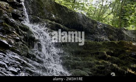 Ein sprudelnder Strom. Kreativ. Große Steine in den Bergen, auf denen eine kalte Quelle auf die Steine trifft. Hochwertige 4K-Aufnahmen Stockfoto