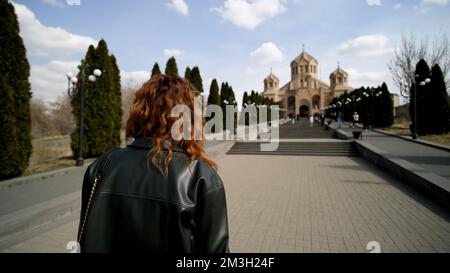 Eine Reisende Frau, die in Richtung Saint Gregory geht, der Illuminator Cathedral. Aktion. Die Kathedrale von Eriwan und die Treppen sind mit wachsenden Tubha-Bäumen auf blu dekoriert Stockfoto