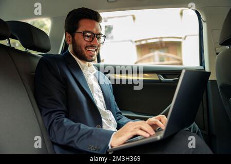 Attraktiver Geschäftsmann im Anzug, der mit einem Laptop unterwegs ist Stockfoto