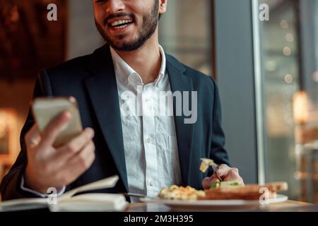 Ein lächelnder indischer Geschäftsmann im Anzug telefoniert während der Mittagspause im Café Stockfoto