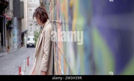 Wunderschöne Porträts neben der Graffiti-Mauer. Action. Stilvolle Leute, die an Straßenkunst-Schießereien mit einer Wand mit leuchtendem Graffiti teilnehmen. Hohe Qualität Stockfoto