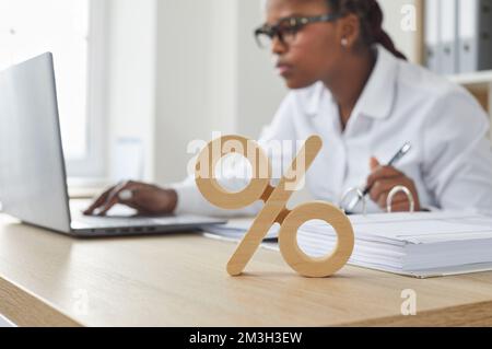 Prozentangabe am Schreibtisch, Geschäftsfrau arbeitet im Hintergrund an einem Notebook Stockfoto