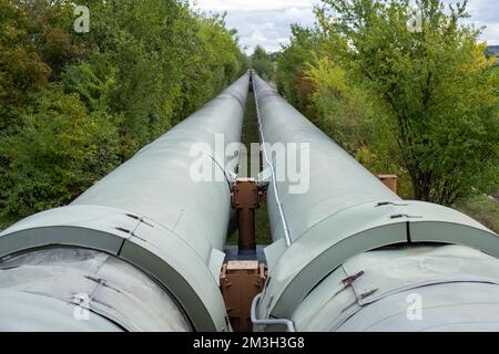 Infrastruktur für den Transfer von Wärmeenergie. Zentralheizungsrohre in einem thermischen Schutzmantel aus Metall, der in europa über dem Boden verlegt ist. Stockfoto