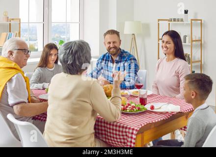 Große Familieneltern, Großeltern und Kinder unterhalten sich zu Mittag und sitzen zu Hause am Tisch. Stockfoto