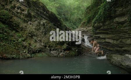 Ein Spaziergang auf den Felsen mit einem sprudelnden Bach. Kreativ. Kleine Wasserfälle mit kaltem Wasser, wo Touristen schwimmen und spazieren gehen. Hochwertige 4K-Aufnahmen Stockfoto