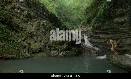 Ein Spaziergang auf den Felsen mit einem sprudelnden Bach. Kreativ. Kleine Wasserfälle mit kaltem Wasser, wo Touristen schwimmen und spazieren gehen. Hochwertige 4K-Aufnahmen Stockfoto