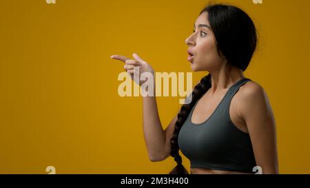 Schockierte, erstaungene, emotionale, indische Frau mit gelbem Studiohintergrund, die auf die Seite zeigt, um leere COPE-Weltraum-Werbung zu zeigen erstaunlich Stockfoto