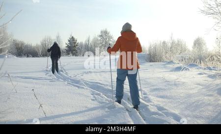 Slow Motion Rückblick auf Skifahrer, die an einem frostigen Wintertag den schneebedeckten Pfad hinunterfahren. Kreativ. Menschen wandern und bewegen sich durch Schnee Stockfoto