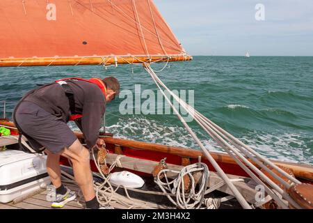 Ein Besatzungsmitglied, das an Bord des traditionellen Gaff Cutters „Jolie Brise“ arbeitet und im Wind in Solent, Hampshire, Großbritannien, läuft Stockfoto