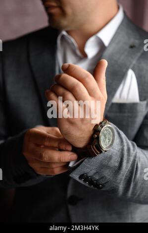 Ein Mann zieht eine Uhr an und passt sie an seinem Handgelenk an, klassischer Männerstil. Stockfoto