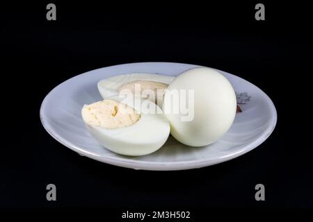Eine Nahaufnahme hartgekochter Eier auf einer weißen Platte, isoliert auf schwarzem Hintergrund Stockfoto