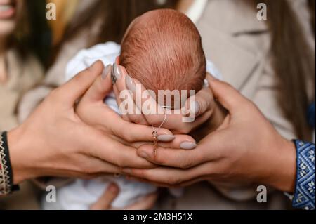 Das Sakrament der Taufe eines Kindes in der Kirche, halten die Eltern den Kopf und das Kreuz des Kindes, die Hände der Eltern und des Kindes. Stockfoto