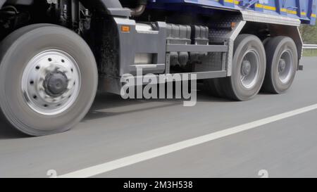 Der Prozess des Frachttransports. Szene: Ein riesiger Truck mit einer Frachtkabine, der in einem grünen Wald entlang der Autobahn rast. Hochwertige 4K-Aufnahmen Stockfoto