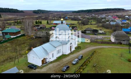 Ein kleiner weißer Tempel. Die Aussicht von der Drohne. Clip. Eine grüne, trübe Landschaft mit grauem Himmel, wo es eine Kirche mit kleinen goldenen Kuppeln und klein gibt Stockfoto