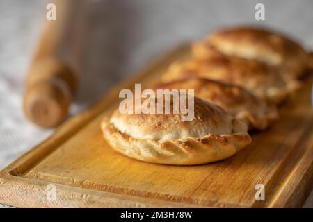 Nahaufnahme von gebackenen argentinischen Empanadas auf einem Brett. Stockfoto