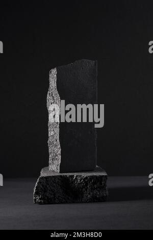 Ein schöner Sockel aus schwarzen Steinen auf dunklem Hintergrund mit Platz für Ihr Produkt Stockfoto