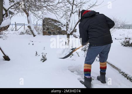 Ein älterer Mann entfernt Schnee vom Gartenweg. Stockfoto