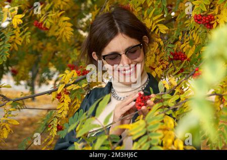 Porträt einer glücklichen, attraktiven Frau in dunkler Sonnenbrille, eingerahmt vom herbstroten Rowan Stockfoto