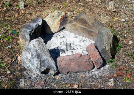 Ein erloschener roter Backsteinherd mit verkohltem Brennholz im Wald aus nächster Nähe. Stockfoto