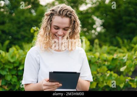 Eine Landwirtin, die Weinberge untersucht und Daten vom Tablet in die Cloud sendet. Intelligente Landwirtschaft und digitale Landwirtschaft. Internet-Technologie. Qualität Stockfoto