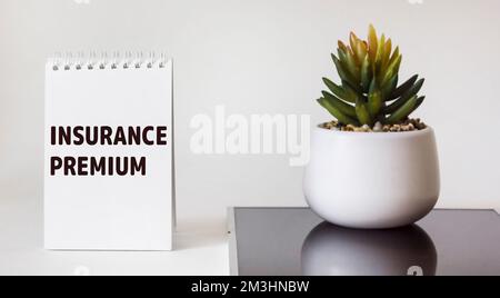 TEXT FÜR VERSICHERUNGSPRÄMIE auf Notizblock mit Kaktusblume auf weißem und schwarzem Hintergrund Stockfoto