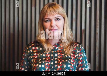 Unschärfe blonde junge Frau Porträt drinnen. Holzlinien im Hintergrund. Lifestyle-Frauen. Vertikal. 40s Jahre Frauen. Lächelnde Frau. Unscharf. Stockfoto