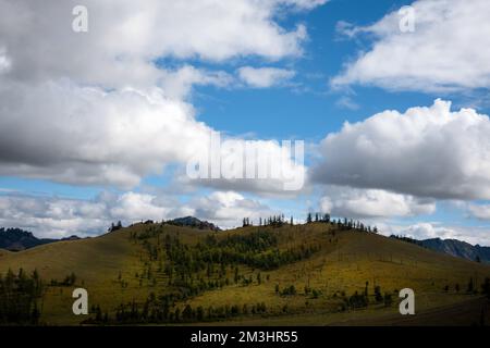 Wunderschöne Bergausläufer, Wolken und blauer Himmel im Hintergrund. Mongolische Berglandschaft an einem bewölkten Tag. Stockfoto