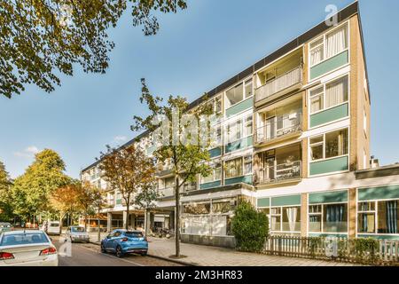 Ein Apartmentgebäude mit Autos, die auf der Seite der Straße davor geparkt sind, und Bäumen, die den Bürgersteig säumen Stockfoto