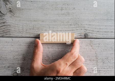 Top view of male hand placing a blank wooden peg on white textured wooden background. Stockfoto