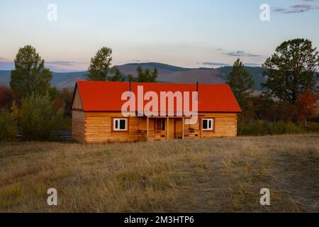 Haus auf dem Land mit den Bergen im Hintergrund. Bauernhütte im ländlichen Land, umgeben von Wäldern und Hügeln mit schneebedeckten Decken. Stockfoto