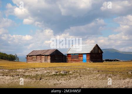 Haus auf dem Land mit den Bergen im Hintergrund. Bauernhütte im ländlichen Land, umgeben von Wäldern und Hügeln mit schneebedeckten Decken. Stockfoto