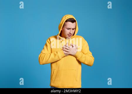 Junger Mann in gelbem Sweatshirt mit Händen auf der Brust Stockfoto