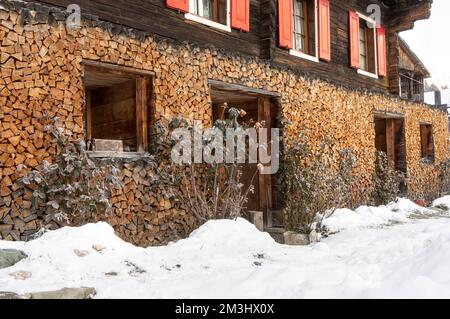 Brennholz an der Außenwand eines traditionellen alpinen Hauses im Winter Stockfoto