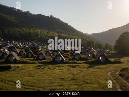 Süße kleine Dorfhäuser am Fuße eines Hügels an einem sonnigen Tag. Ländliches Nomadenleben, wunderschöne Berge im Hintergrund, goldene Stunde. Stockfoto