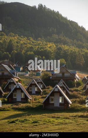 Süße kleine Dorfhäuser am Fuße eines Hügels an einem sonnigen Tag. Ländliches Nomadenleben, wunderschöne Berge im Hintergrund, goldene Stunde. Stockfoto