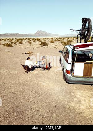 Mann und Frau arbeiten per Fernzugriff von ihrem Wohnmobil aus, indem sie Inhalte und Strategien in der Wildnis eines trockenen Sees planen Stockfoto