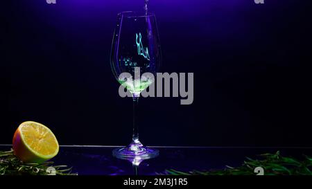 Nahaufnahme des Gießens eines grünen Cocktailgetränks in einem transparenten Glas, das auf der Theke steht. Clip. Die Bar ist mit grünen Blättern und oran dekoriert Stockfoto