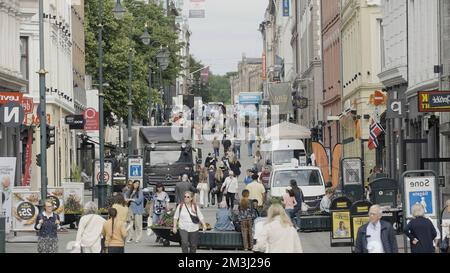 Norwegen, Oslo - 27. Juli 2022: Überfüllte Stadtstraße mit vielen Geschäften und Restaurants. Aktion. Belebte Straße mit Menschen und Autos Stockfoto