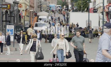 Norwegen, Oslo - 27. Juli 2022: Überfüllte Stadtstraße an einem Sommertag. Aktion. Menschen, die an Gebäuden entlang gehen Stockfoto