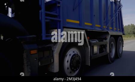 Ein riesiger blauer Truck. Szene: Ein Lkw mit blauer Karosserie, der langsam entlang der Autobahn fährt, befindet sich neben einem grünen Wald. Hochwertige FullHD-Aufnahmen Stockfoto